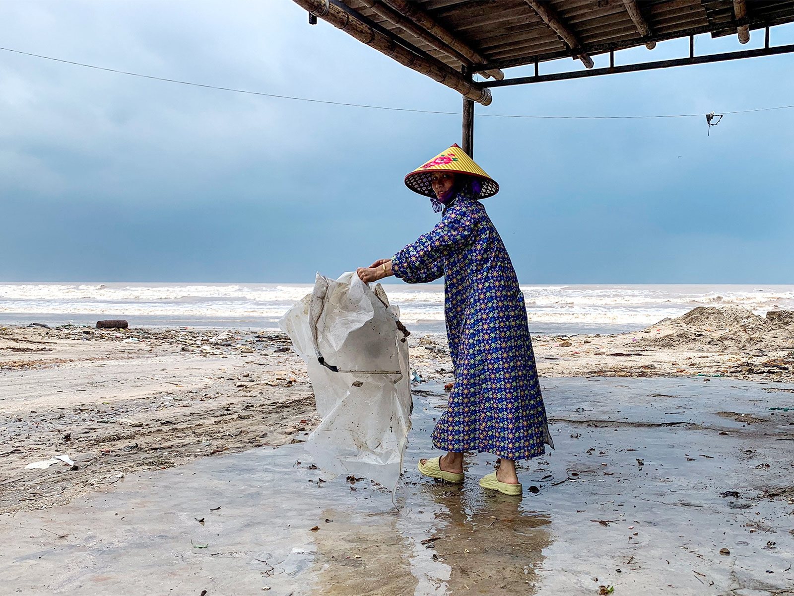 A woman wearing a raincoat collects a plastic bag near a beach as Typhoon Bualoi nears (Photo/ Reuters)