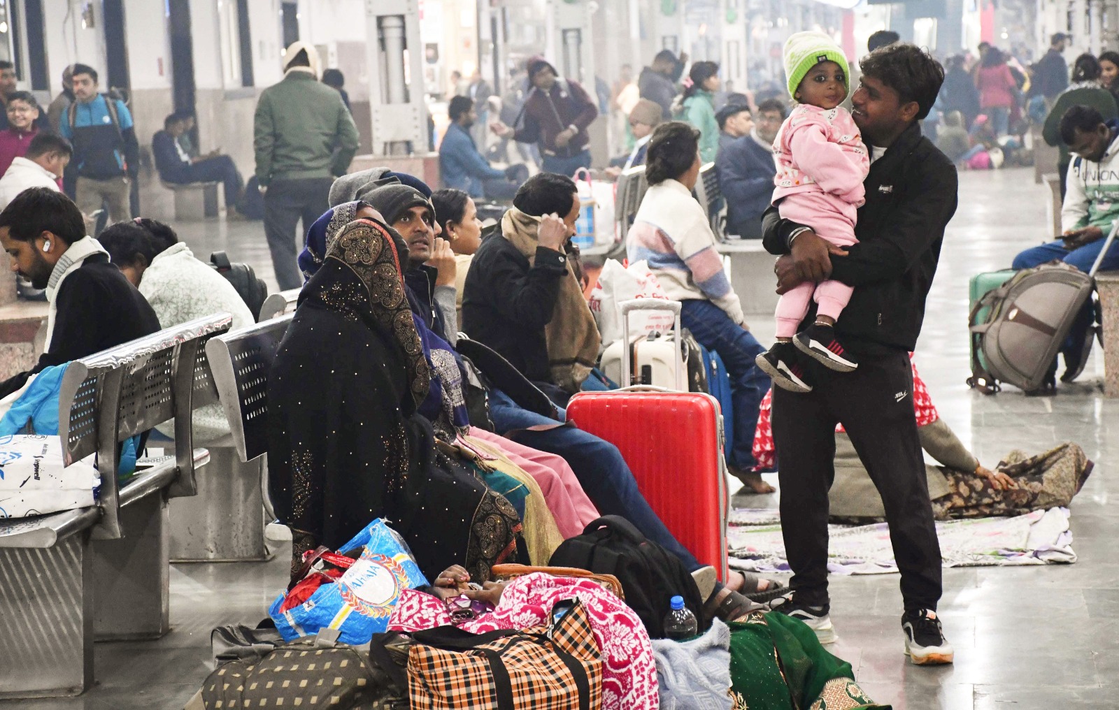 Passengers wearing warm clothes wait for their train at the railway station on a cold winter morning, in Prayagraj (Photo/ANI)