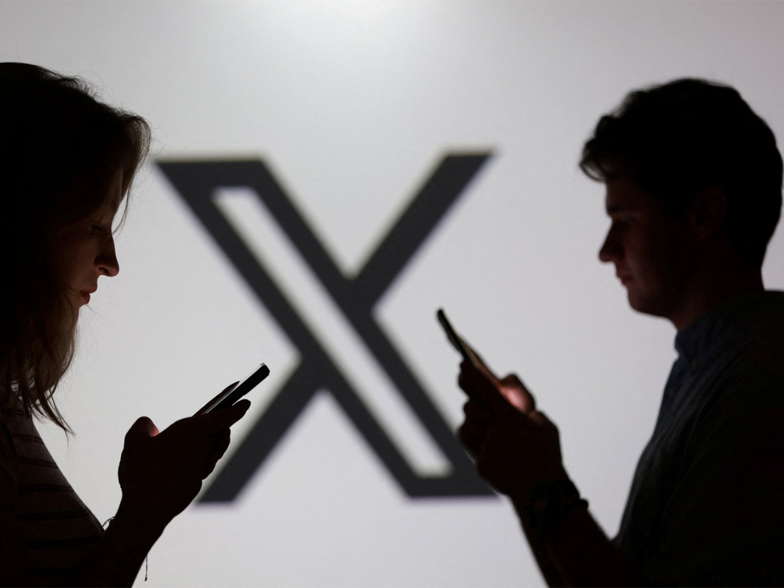 Teenagers pose for a photo while holding smartphones in front of a X logo (Photo/ Reuters)