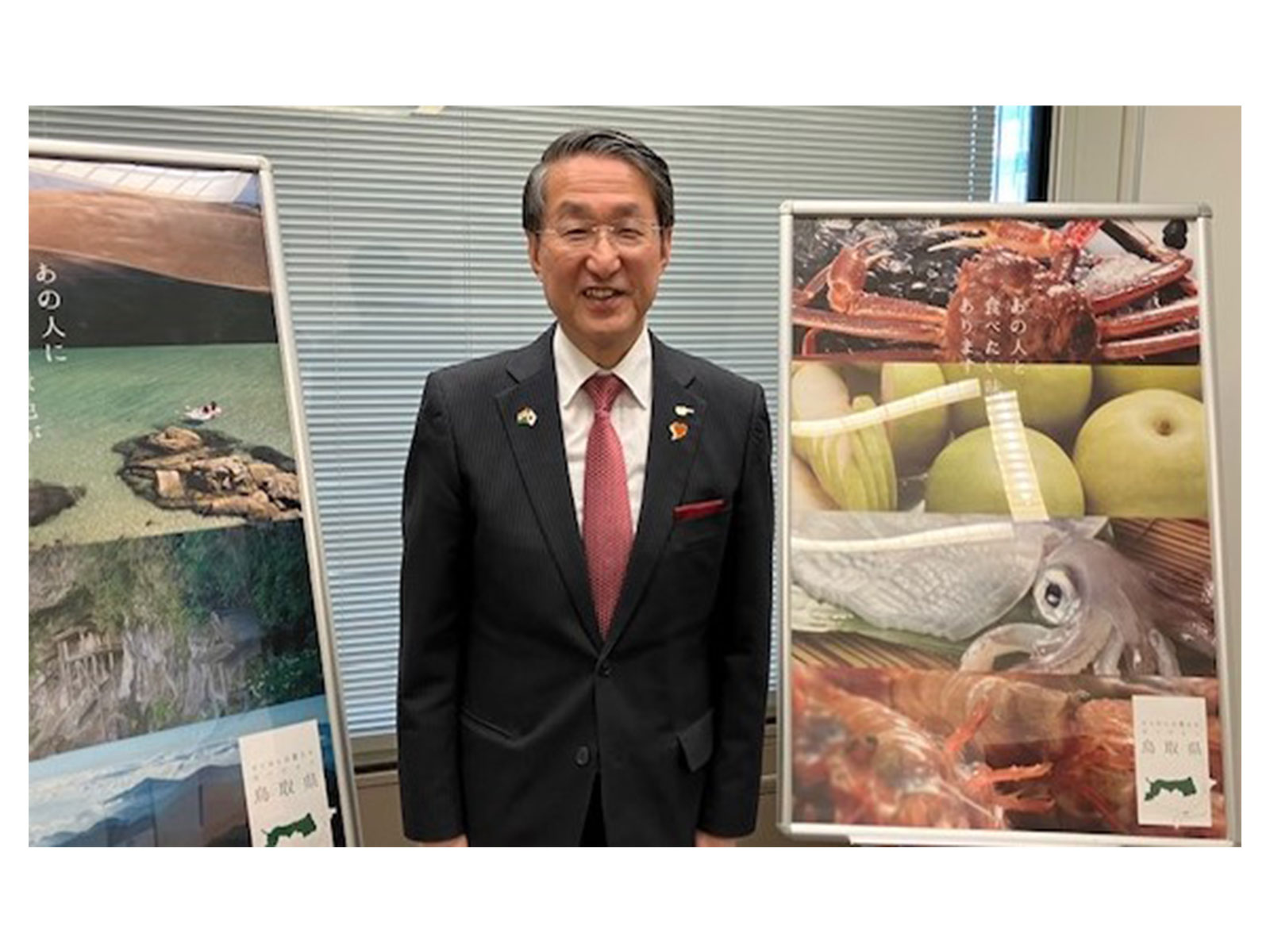 Tottori Prefecture Governor Shinji Hirai poses beside display boards showcasing local seafood and scenic landscapes (Photo/ANI) 