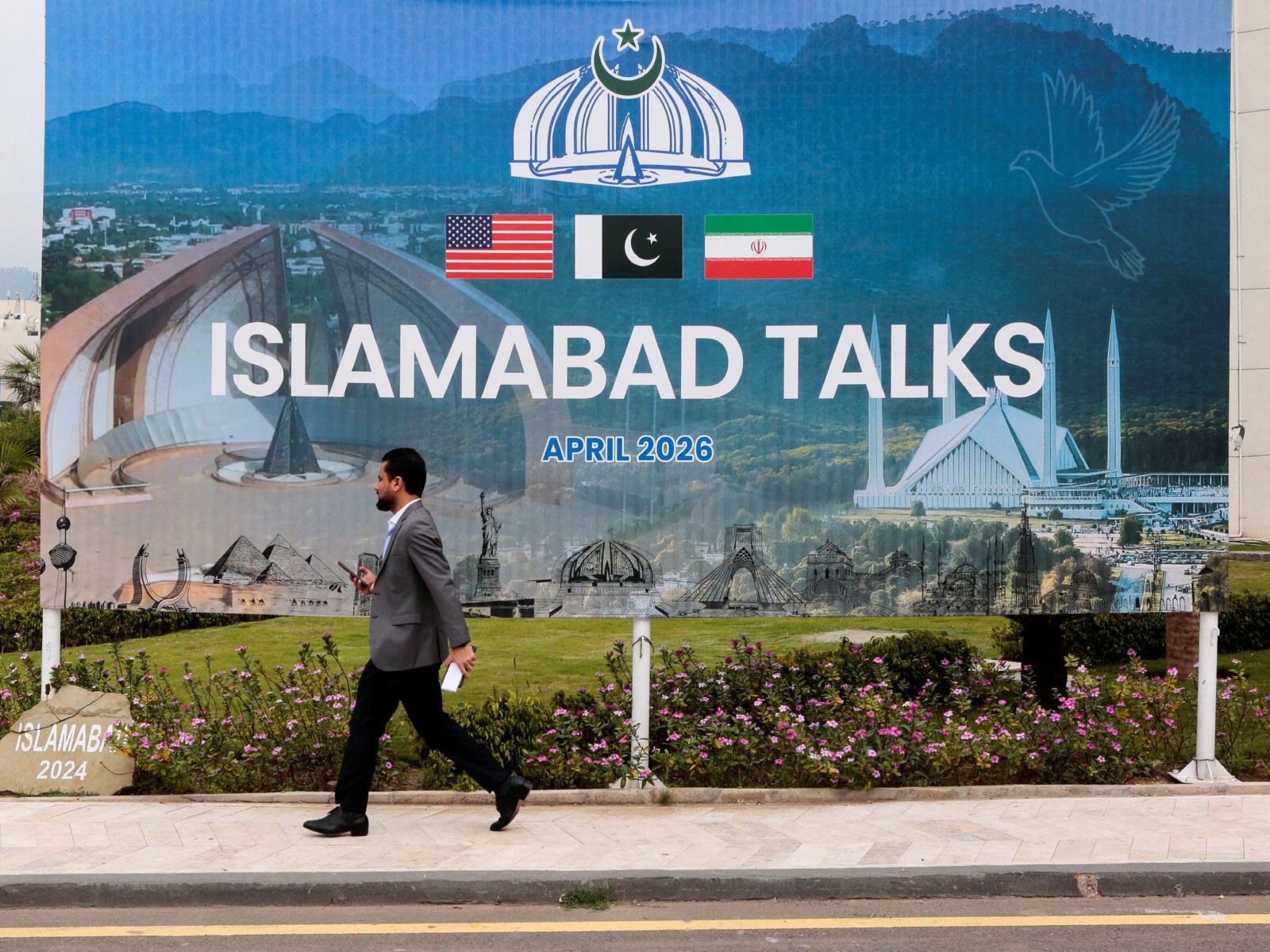 A passerby walks by a billboard near the media centre in Islamabad, where delegations from the United States and Iran are set to engage in peace talks. (File Photo/Reuters)
