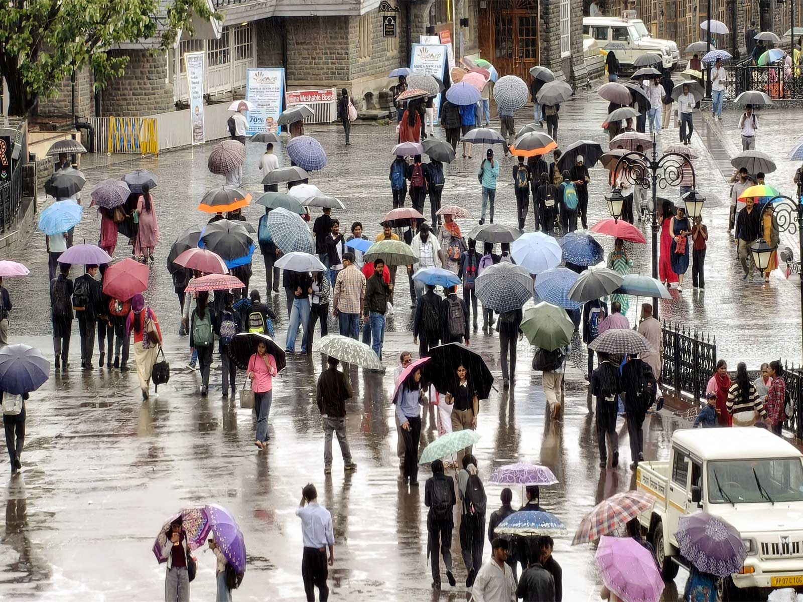 People cover themselves with umbrellas as they walk amid rainfall (Photo/ANI)