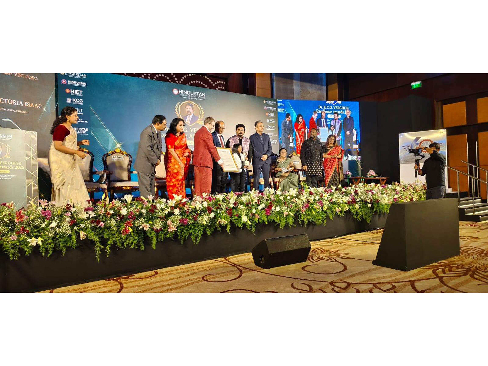 Victoria Isaac collects her citation at the Dr. K.C.G. Verghese Excellence Awards 2026 in Chennai. The screen at the left of the stage carried her name and her stage name, Victoriastic