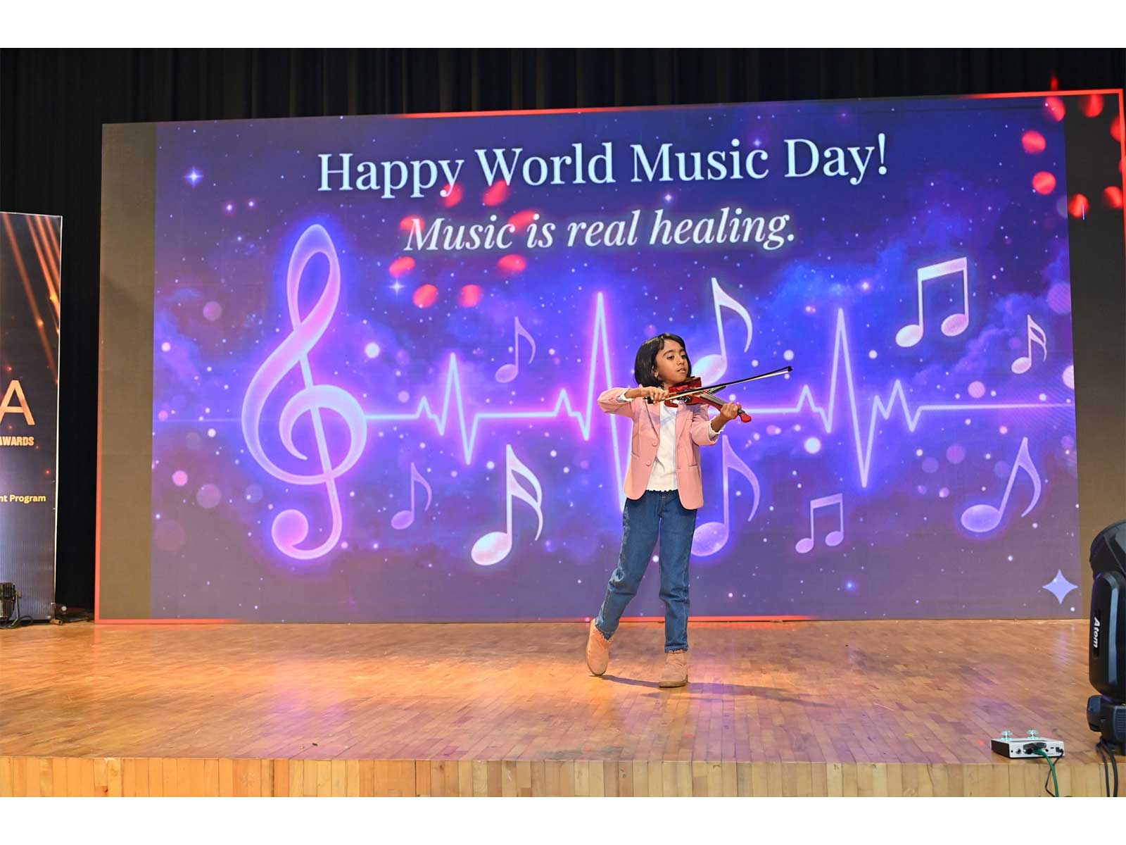 Victoria Isaac performing at the South India Women Achievers Awards 2026, Jawaharlal Nehru Centre auditorium, Bengaluru. The screen behind her carried the line "Music is real healing."