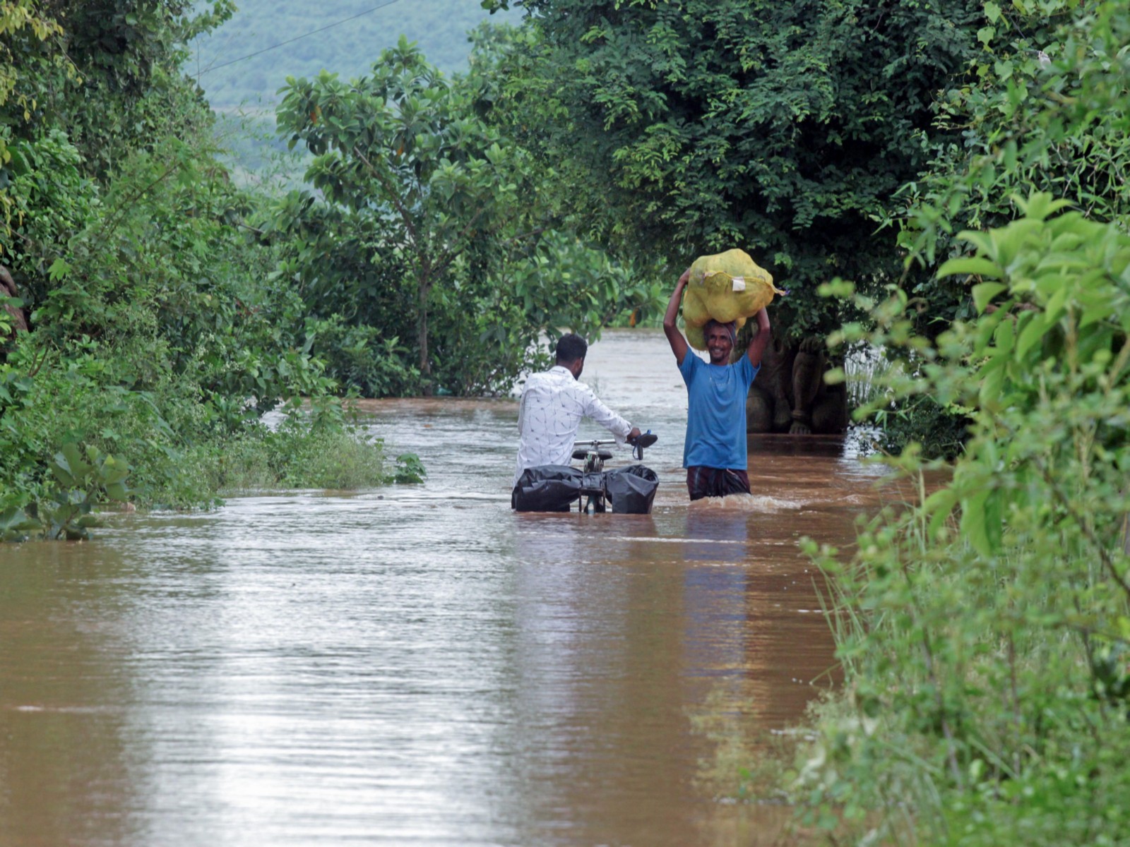 People wade through a flood water of the Mahanadi river entered the villages below Cuttack and Banki districts in Odisha (Photo/ANI)