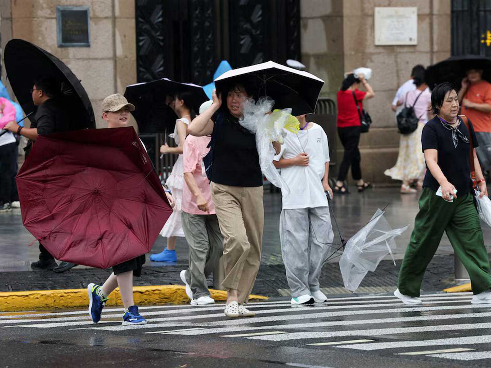 A person carrying a damaged umbrella as pedestrians cross a road amid strengthening winds ahead of Typhoon Dolphin's arrival in Shanghai, China. (Photo/Reuters)