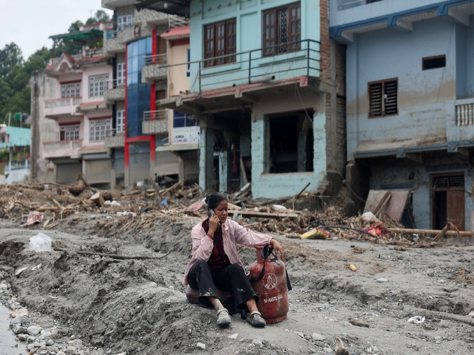 A woman speaks on a phone as she sits next to a gas cylinder at the site of flash floods and mudslides, in Devighat (File Photo/ANI) 