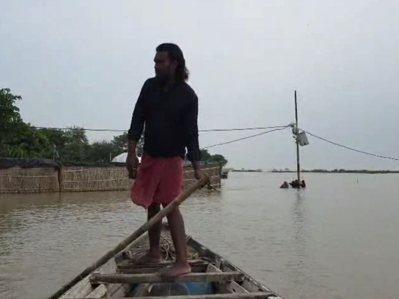 A man navigates a small boat through a flooded area near submerged houses and power lines (Photo/ANI)