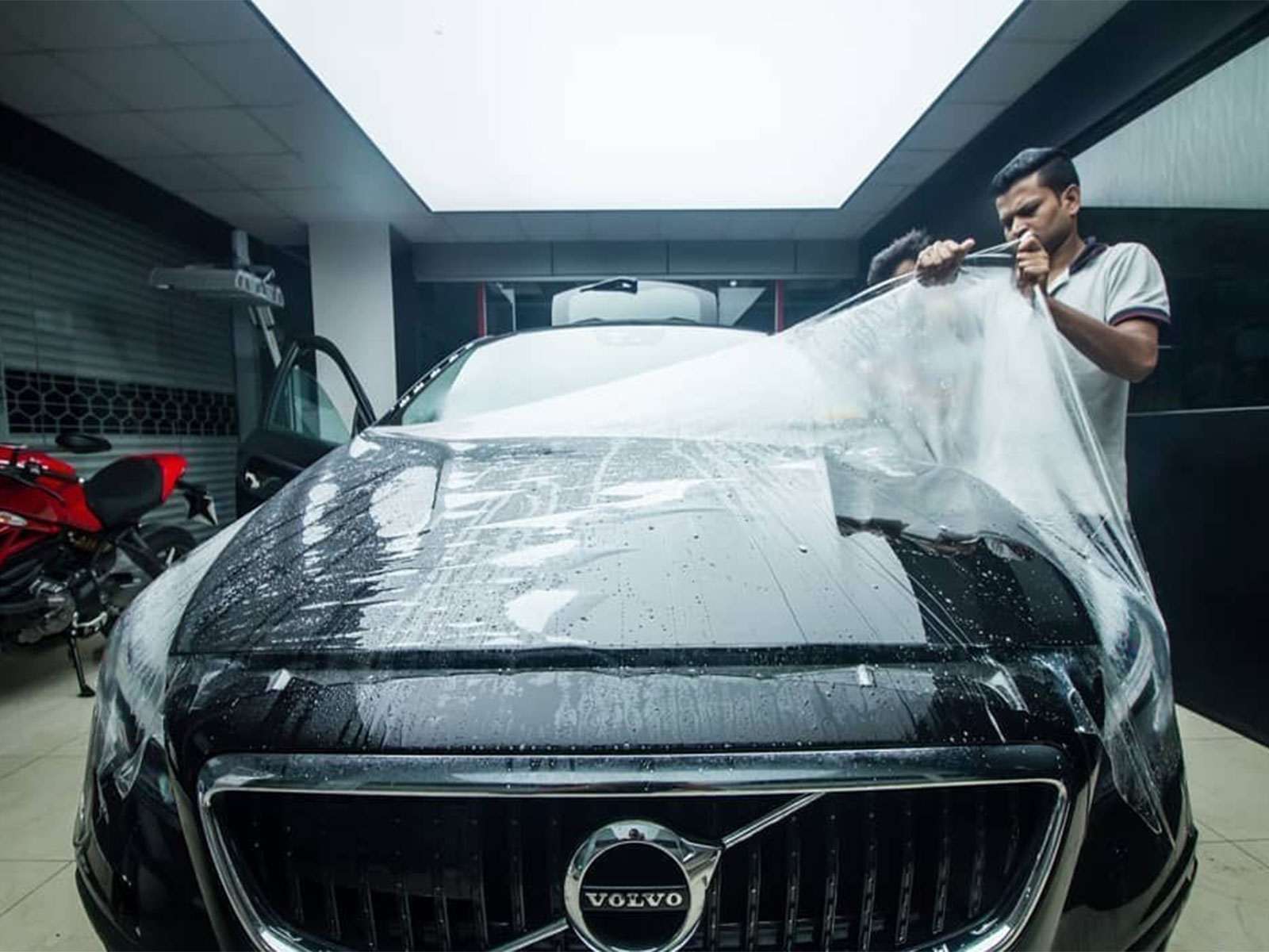 A black Volvo car being covered with a transparent paint protection film (PPF).