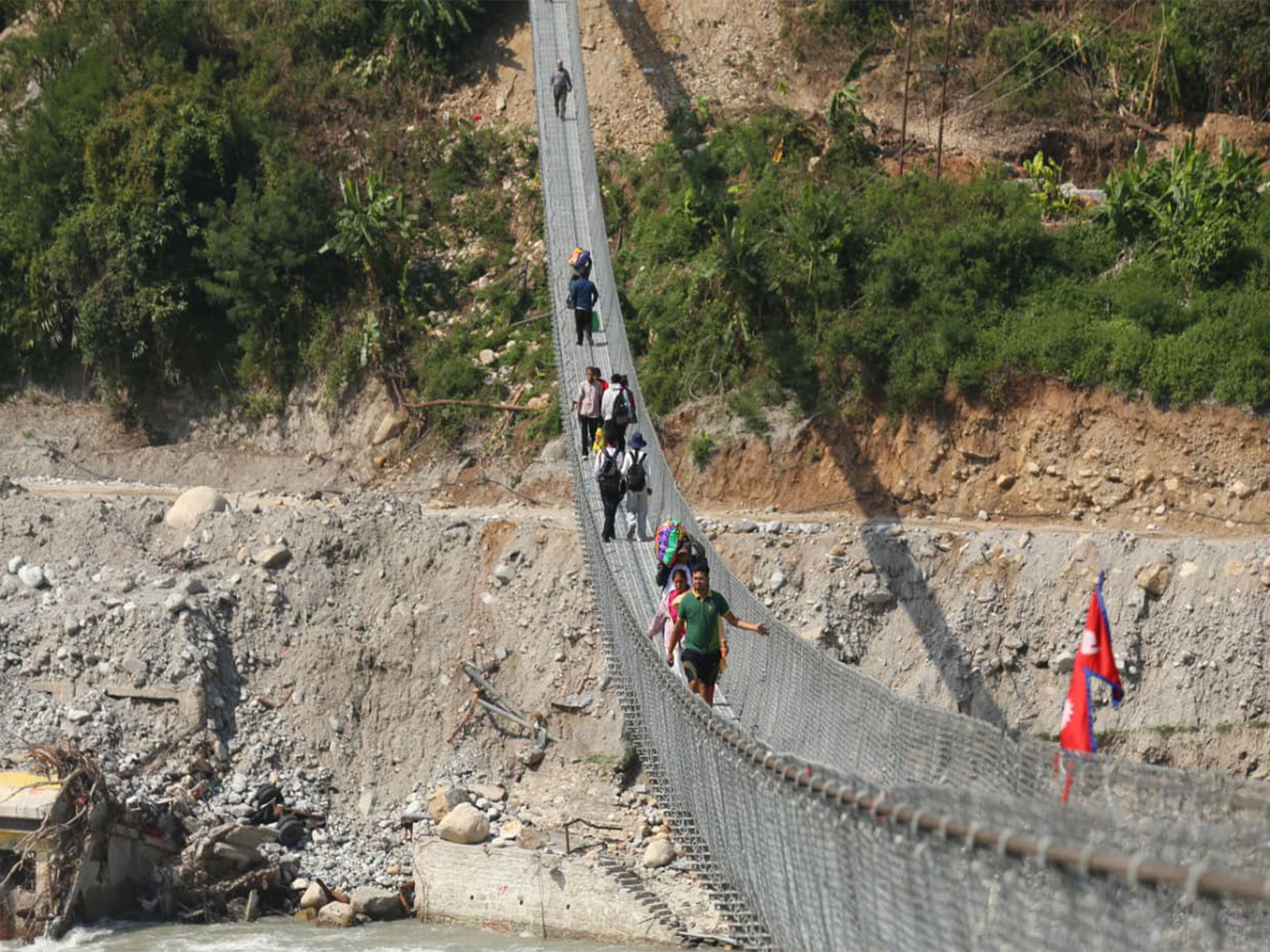 People walk across a suspension bridge in Devighat, Nuwakot district, amid the aftermath of the August 26 flash flood. (Photo/ANI)