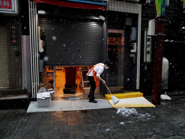 A shop employee wearing a protective face mask following an outbreak of COVID-19 tries to remove snow in Tokyo, Japan March 29, 2020. A shop employee wearing a protective face mask following an outbreak of COVID-19 tries to remove snow in Tokyo, Japan March 29, 2020.